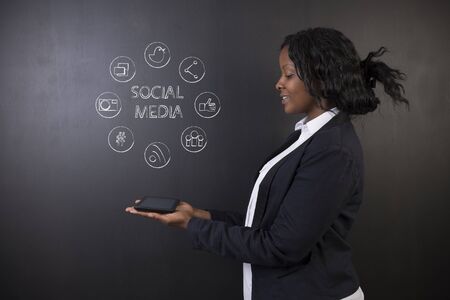 South African or African American woman teacher or student holding tablet computer showing social media chalk concept on a blackboard backgroundの写真素材