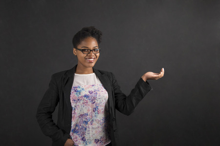 South African or African American black woman teacher or student holding her hand out to the side standing against a chalk blackboard background insideの写真素材