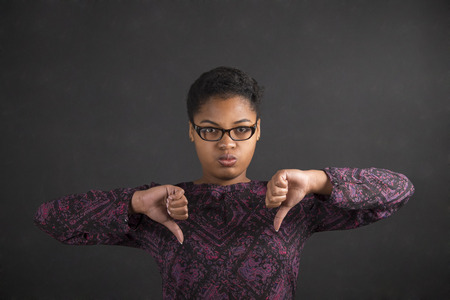 South African or African American black woman teacher or student with thumbs down hand signal on a chalk black board background insideの写真素材