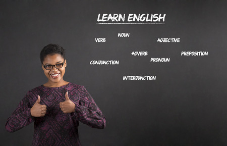 South African or African American black woman teacher or student with a thumbs up hand signal teaching English standing against a chalk blackboard background insideの写真素材