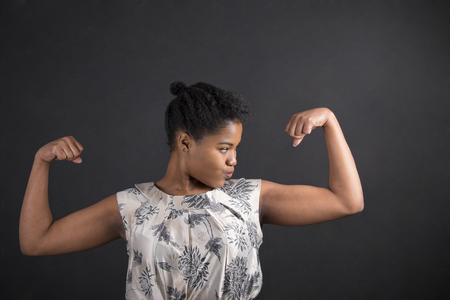 South African or African American black woman teacher or student with strong muscular arms standing against a chalk blackboard background insideの写真素材