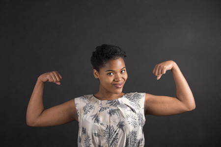South African or African American black woman teacher or student with strong muscular arms standing against a chalk blackboard background insideの写真素材