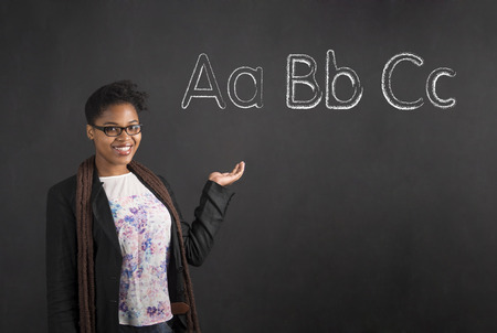 South African or African American black woman teacher or student showing or displaying the ABC alphabet standing against a chalk blackboard background insideの写真素材