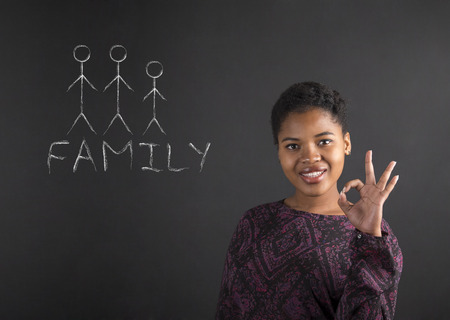 South African or African American black woman teacher or student holding up a perfect hand signal with family diagram on a chalk blackboard background insideの写真素材