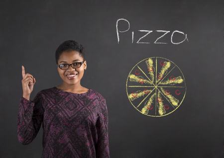 South African or African American black woman teacher or student with a good idea for pizza standing against a chalk blackboard background insideの写真素材