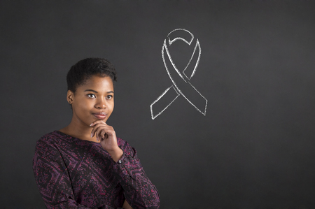 South African or African American black woman teacher or student with her hand on her chin whilst thinking about illness awareness standing against a chalk blackboard background insideの写真素材