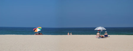 Beach panoramic beach landscape with 3 groups of people sitting with open sunshadesの写真素材