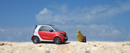 Red smart car parked on a ground crossing with the driver outside the car sitting and restingのeditorial素材