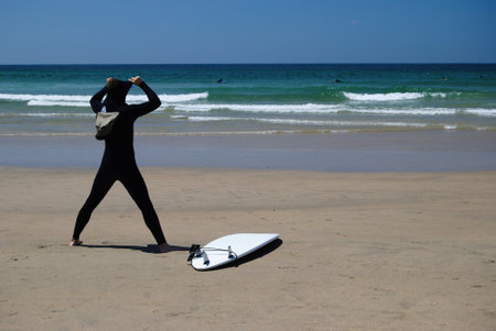 Surfer with surfboard on the sandy beach by the sea.