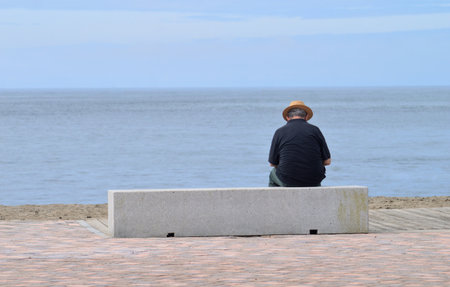 Man sitting on the promenade by the sea looking at the horizonの写真素材