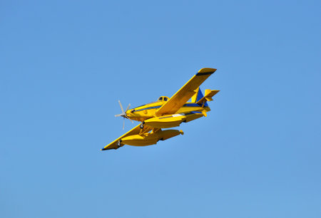 A small yellow plane flies in the blue sky on a sunny day