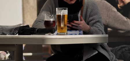 Young woman in a cafe with a glass of beer and a smartphone