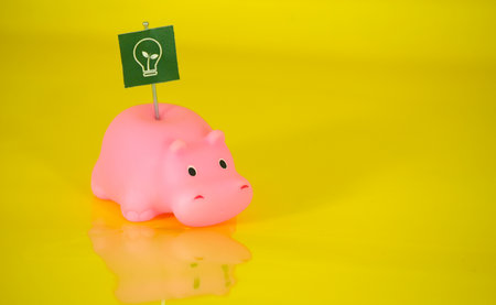 Piggy bank with green sign and lightbulb on yellow backgroundの写真素材