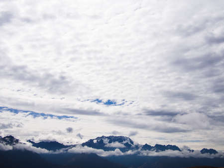 Andes mountain range peeking out of clouds with cloudy sky.の写真素材