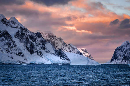 Rugged mountains of Antarctica at sunset or sunrise in pink and orange and cloudy.の写真素材
