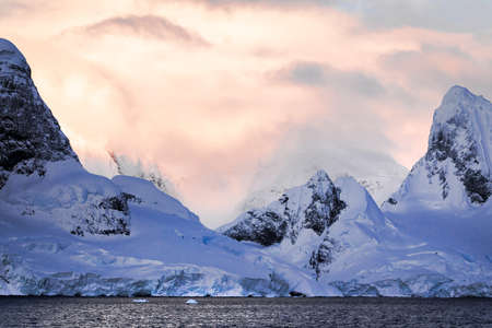 Rugged mountains of Antarctica at sunset or sunrise in pink and orange and cloudy.の写真素材