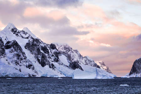 Rugged mountains of Antarctica at sunset or sunrise in pink and orange and cloudy.の写真素材
