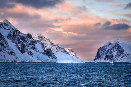 Rugged mountains of Antarctica at sunset or sunrise in pink and orange and cloudy.の写真素材
