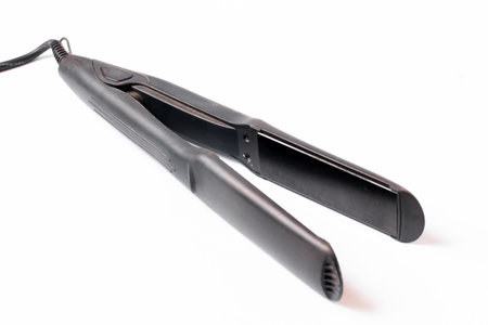 Electric curling iron with ceramic plates isolated on white background. Black hair straightener with ceramic plates isolated on white backgroundの写真素材