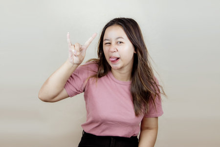 Portrait of a young Asian woman wearing a pink casual t-shirt smiling happily by showing her index finger and little finger.の写真素材