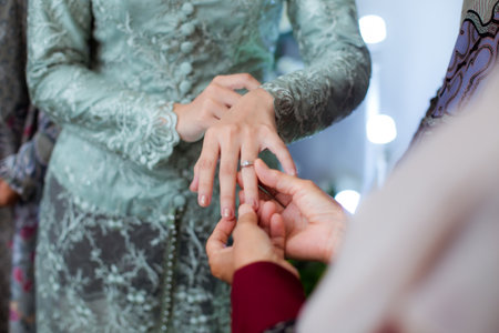 The bride and groom exchange rings at the wedding. A husband and wife put rings on each other's fingers. Holding a wedding ring. Precious metal jewelry for married couples.の写真素材