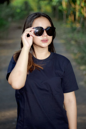 Clothing model. Young Asian woman with sunglasses posing outdoors. Asian woman wearing a plain Navy Blue t-shirt on a background of trees. It was as if he was modeling a plain t-shirt.の写真素材