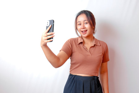 An excited young woman points to her smart phone in her hand, isolated on a white backgroundの写真素材