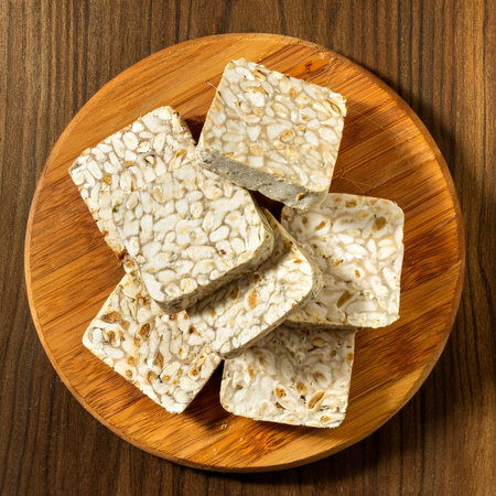 Raw tempeh or tempe on a wooden cutting board, isolated against a wooden backgroundの写真素材