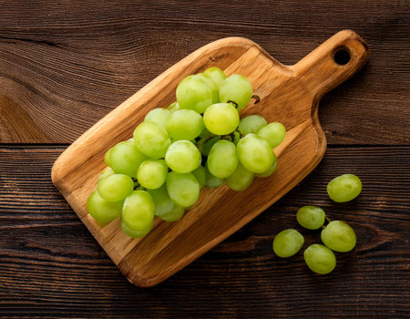 green grapes on a wooden cutting board, isolated against a wooden backgroundの写真素材