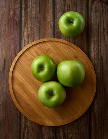 Green apples in wooden cutting board isolated on wooden backgroundの写真素材