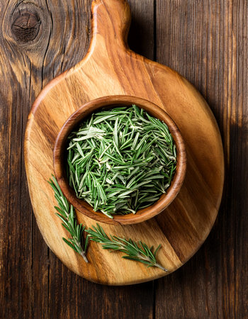 rosemary in wooden bowl on a wooden cutting board, isolated against a wooden backgroundの写真素材