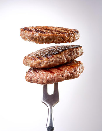 Stack of perfectly grilled hamburger patties with grill marks on vintage fork floating or flying isolated on clean white backgroundの写真素材