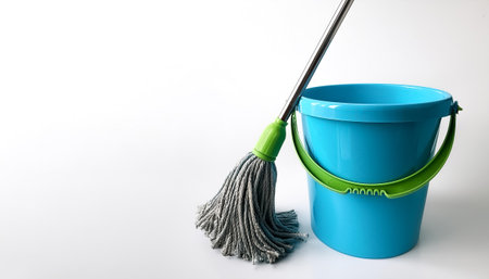 A blue bucket with a green handle sits next to a mop on side position provides copy space for text....