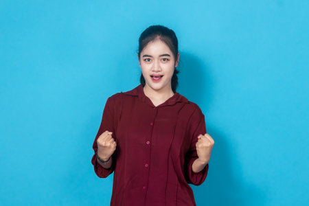 A cheerful woman in a red shirt celebrates with enthusiasm, expressing success and triumph.