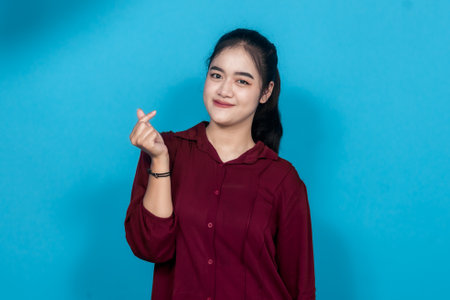 Young woman in a maroon shirt making a hand gesture while smiling, expressing positivity and...