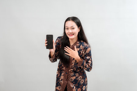 A young woman in a floral patterned outfit smiles while holding a smartphone, showcasing a friendly and engaging demeanor against a neutral background.の写真素材