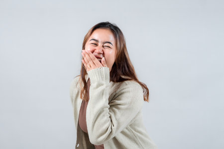 A young woman laughs heartily, covering her mouth with her hand. Her genuine expression of joy and casual style make this image perfect for lifestyle and emotion-related projects.の写真素材