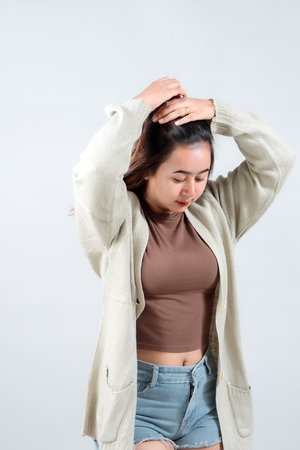 A young woman in a cozy sweater adjusts her hair, showcasing a casual and relaxed style against a neutral background.の写真素材