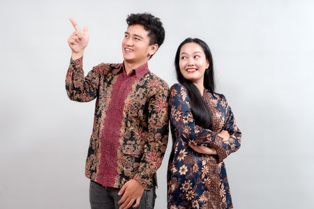 Stylish young Indonesian couple in modern batik shirts. Confident pose against a gray background. Cultural fashion, heritage.の写真素材