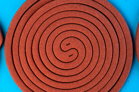 A brown mosquito coil in a spiral shape on a blue background. Insect repellent for outdoor and...