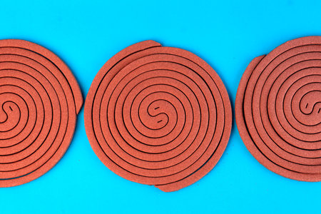 Three brown mosquito coils in a spiral shape on a blue background. Insect repellent for indoor and outdoor use, designed to keep mosquitoes away and provide protection from bites.の写真素材