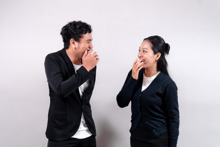 Asian man and woman laughing while covering their mouths, looking at each other. They express...