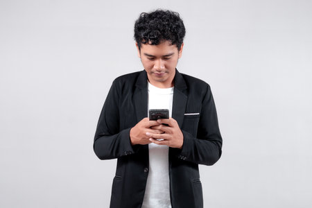 Asian man in black blazer and white t-shirt holding a smartphone with a friendly smile. Isolated on...