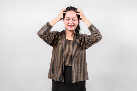 An Indonesian woman wearing a traditional Sorjan or Lurik outfit, expressing stress by holding her head.の写真素材