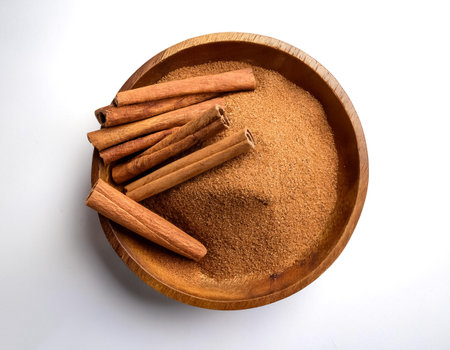 cinnamon sticks and ground cinnamon in a wooden bowl, isolated on a clean white background