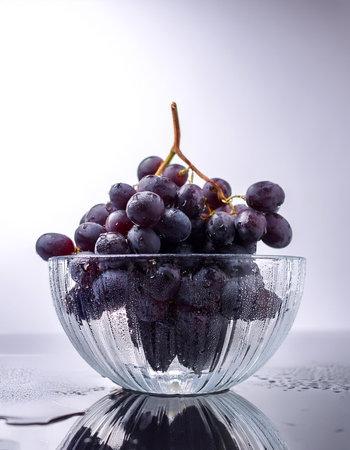 Dark purple grapes are placed in a transparent glass bowl with water dropsの写真素材