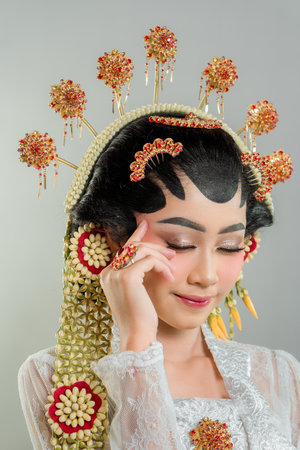 A radiant Indonesian bride in Solo Putri attire poses gracefully. Adorned with a golden headdress, jasmine accessories, and intricate lace kebaya, she smiles charmingly with elegance.の写真素材