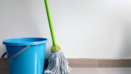 A blue bucket with a green handle sits next to a mop on side position provides copy space for text....