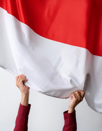 close up of hands holding a large Republic of Indonesia flag and waving it upwards on a white backgroundの写真素材