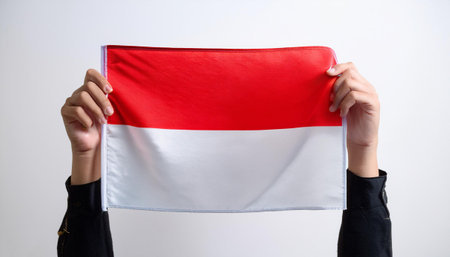 close up of hands holding a large Republic of Indonesia flag and waving it upwards on a white...